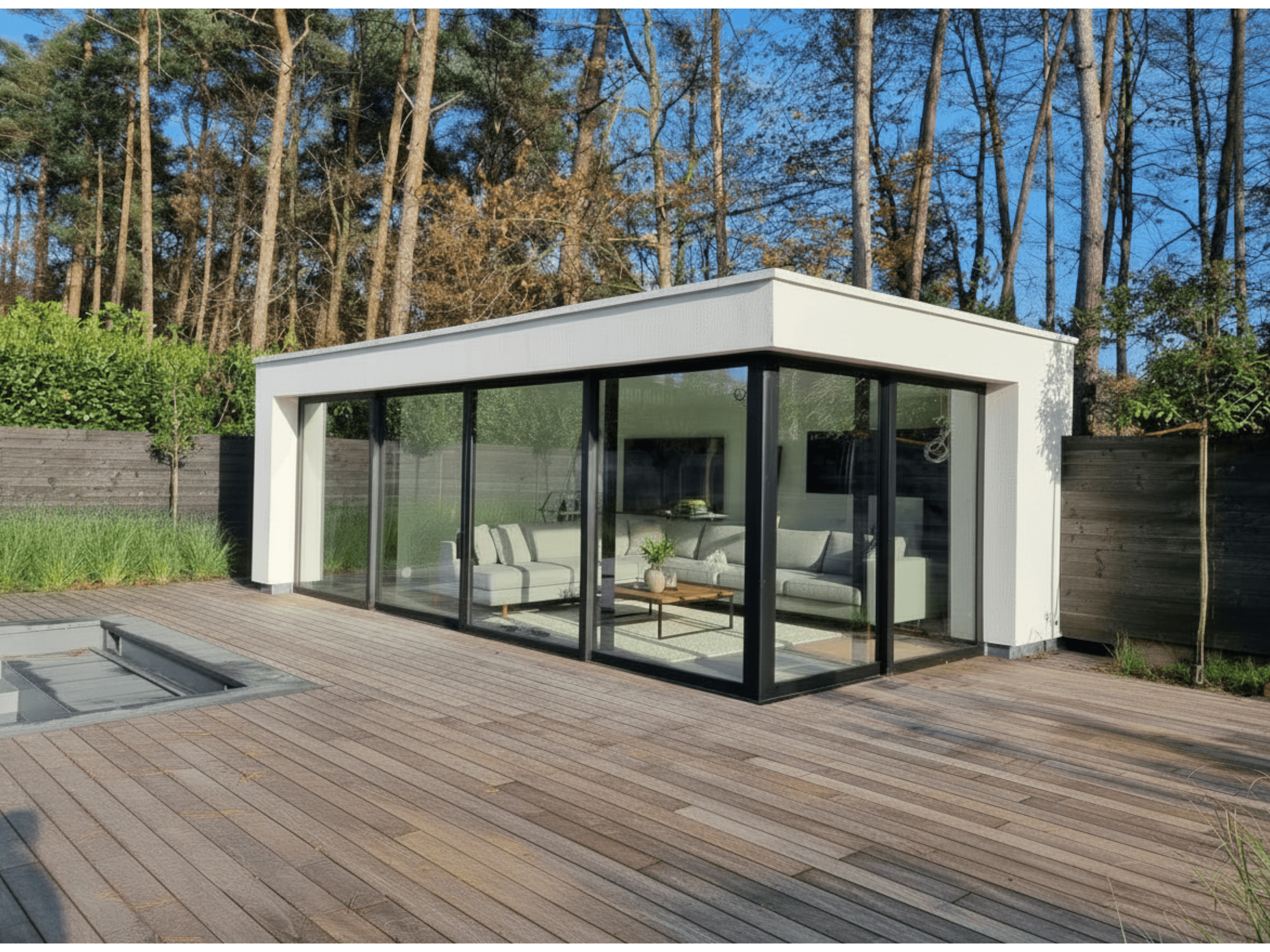 Moderne witte glazen aanbouw met zwarte raamkaders op een houten terras, zicht op woonkamer en bomen op de achtergrond.