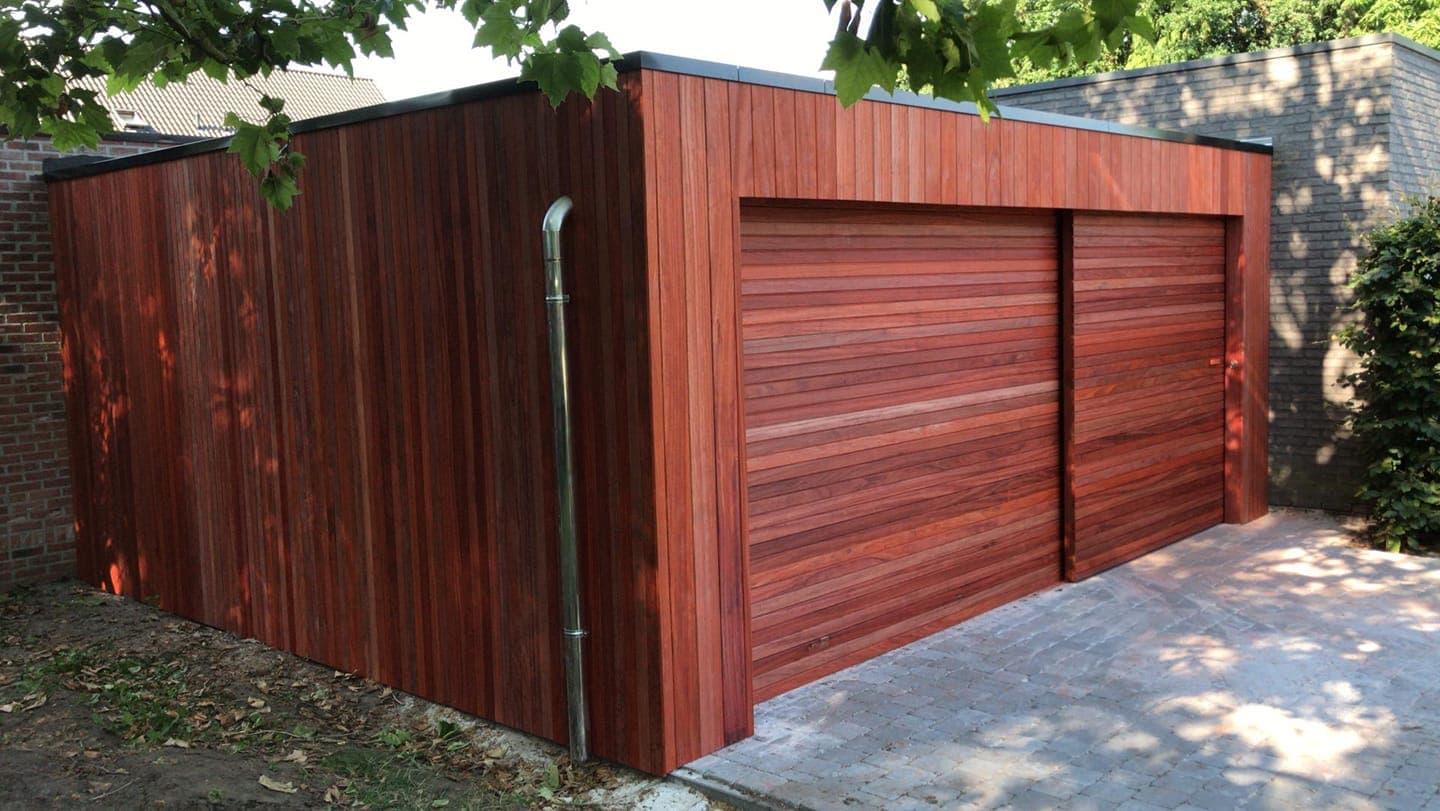 Houten garage met dubbele deuren van roodbruine planken, naast een muur en een betegelde oprit.